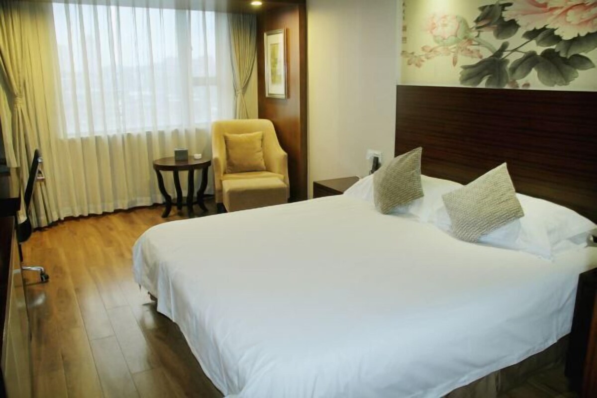 A hotel room with a large bed, a chair, a small table, and a painting on the wall.