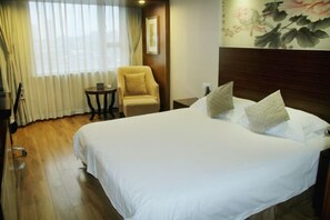 A hotel room with a large bed, a chair, a small table, and a painting on the wall.