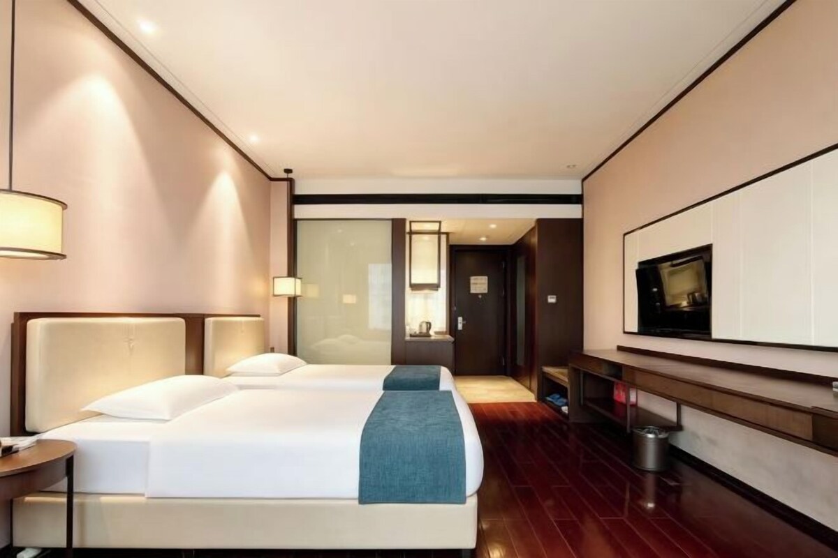 Habitación de hotel con cama, mesitas de noche, televisión y baño visible a través de una puerta de cristal.