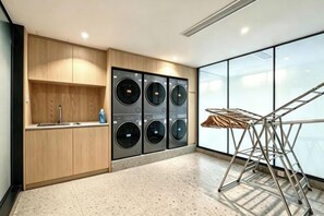 A laundry area with four washing machines, a drying rack, and a wooden cabinet with a sink.