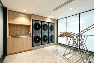 A modern laundry area with four washing machines, a drying rack, and a wooden cabinet with a sink.