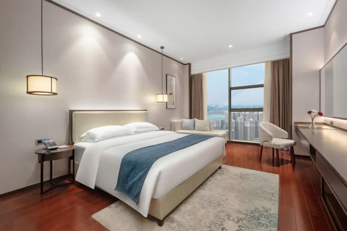 A modern hotel room with a large bed, a desk, a chair, and a view of the city.