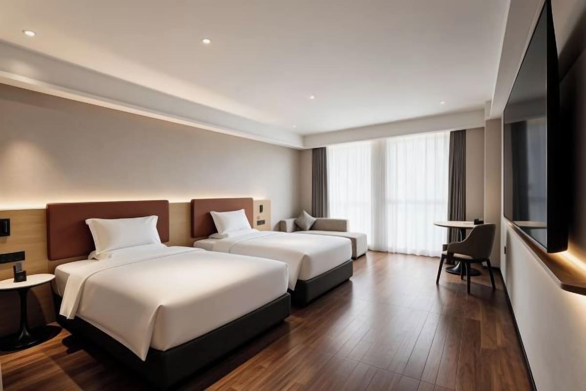 A hotel room with two beds, a desk, and a large window.