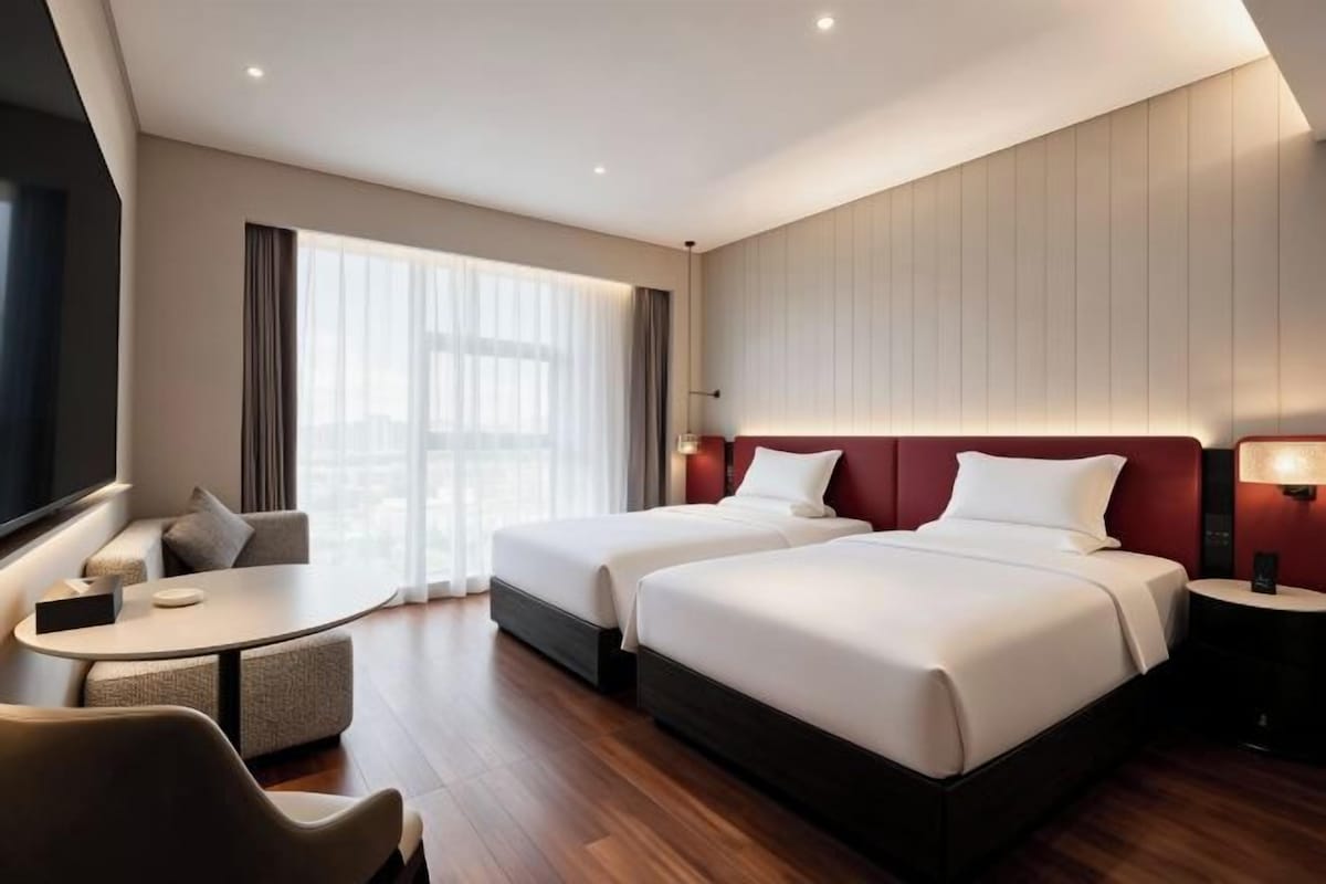 A hotel room with two beds, a desk, and a seating area.