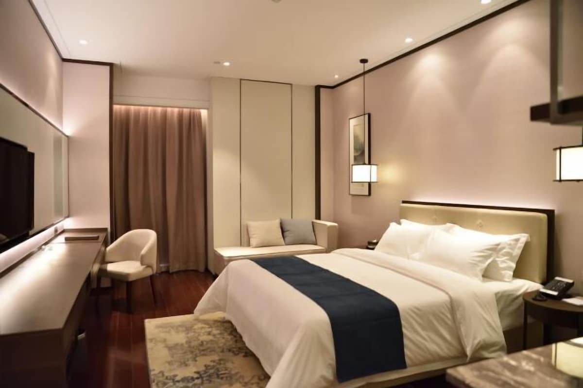 A hotel room with a bed, a desk, a chair, a TV, and a window with curtains.