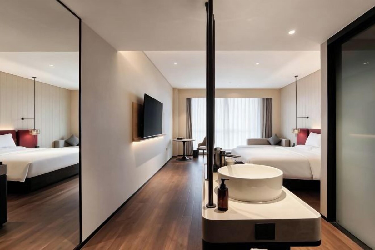 A modern hotel room with a large bed, a round bathtub, a flat-screen TV, and a large window.