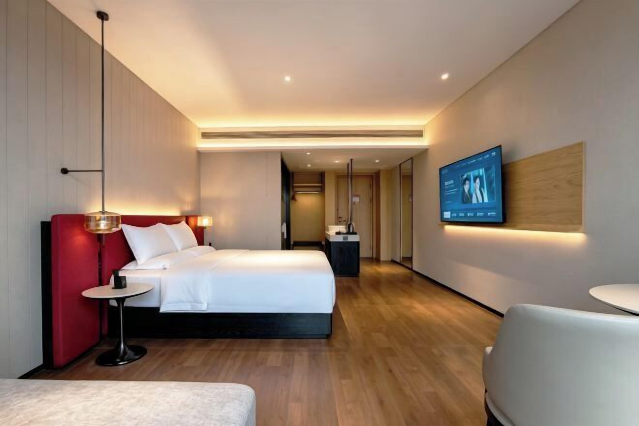 A modern hotel room with a large bed, bedside tables, a TV, and a seating area.