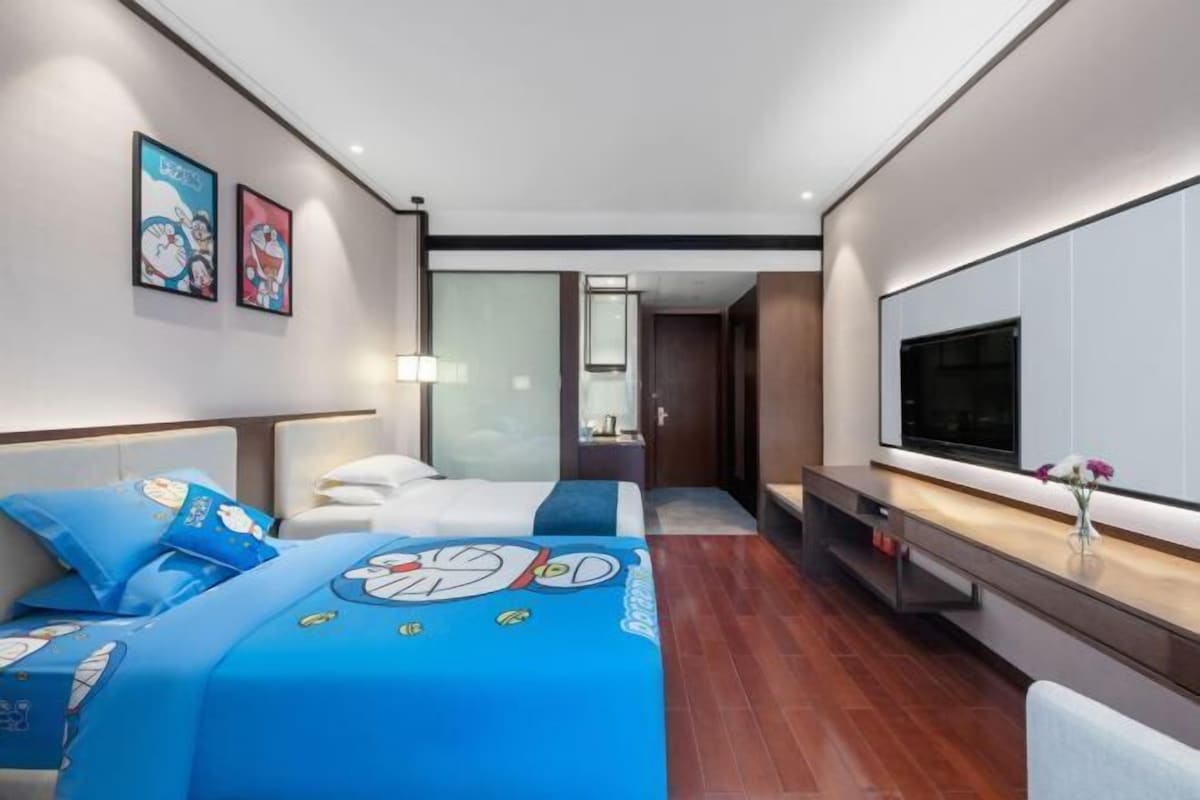 A modern hotel room with a large bed, a TV, and artwork on the walls.