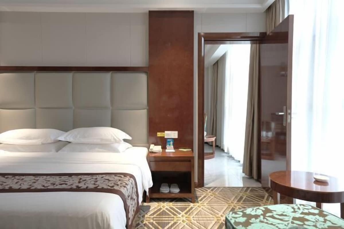 A hotel room with a large bed, a nightstand, a mirror, and a view of the hallway.