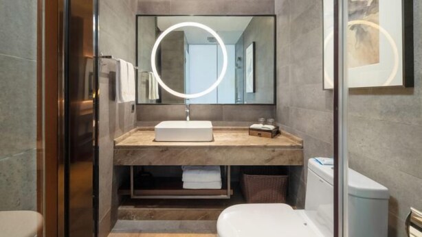 A modern bathroom with a marble vanity, a round mirror with a light, and a toilet. - Yamei Hotel (Xiangtan Youyi) (Xiangtan)