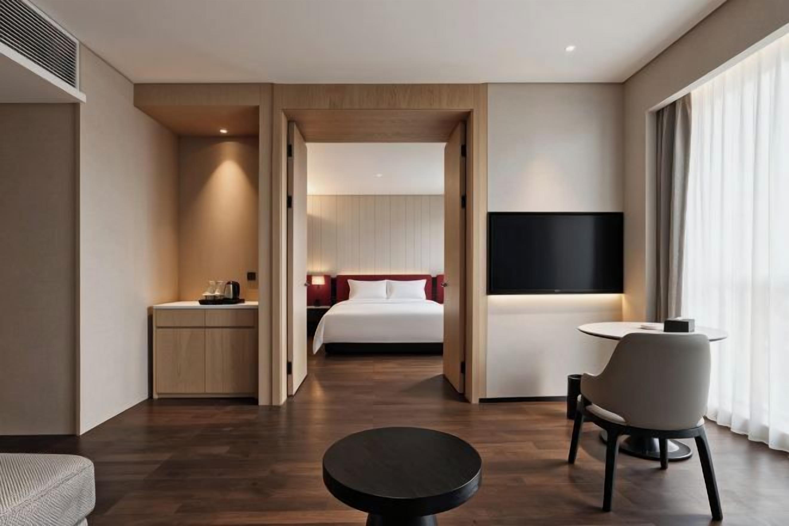 A hotel room with a bed, bedside table, TV, and a seating area with a table and chairs.
