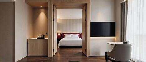 A hotel room with a bed, bedside table, TV, and a seating area with a table and chairs.
