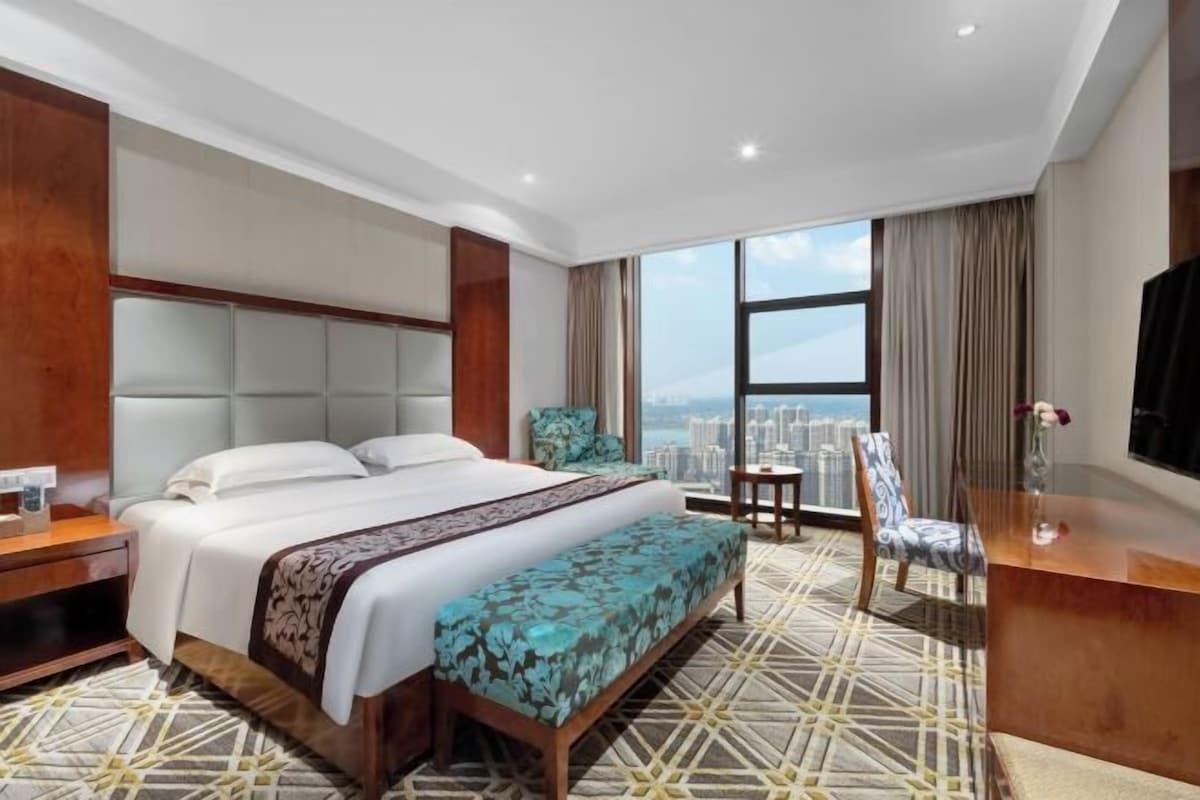 A hotel room with a large bed, a desk, a chair, and a view of a cityscape.