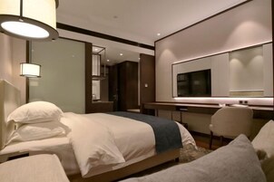 A modern hotel room with a large bed, a desk, a chair, and a television.