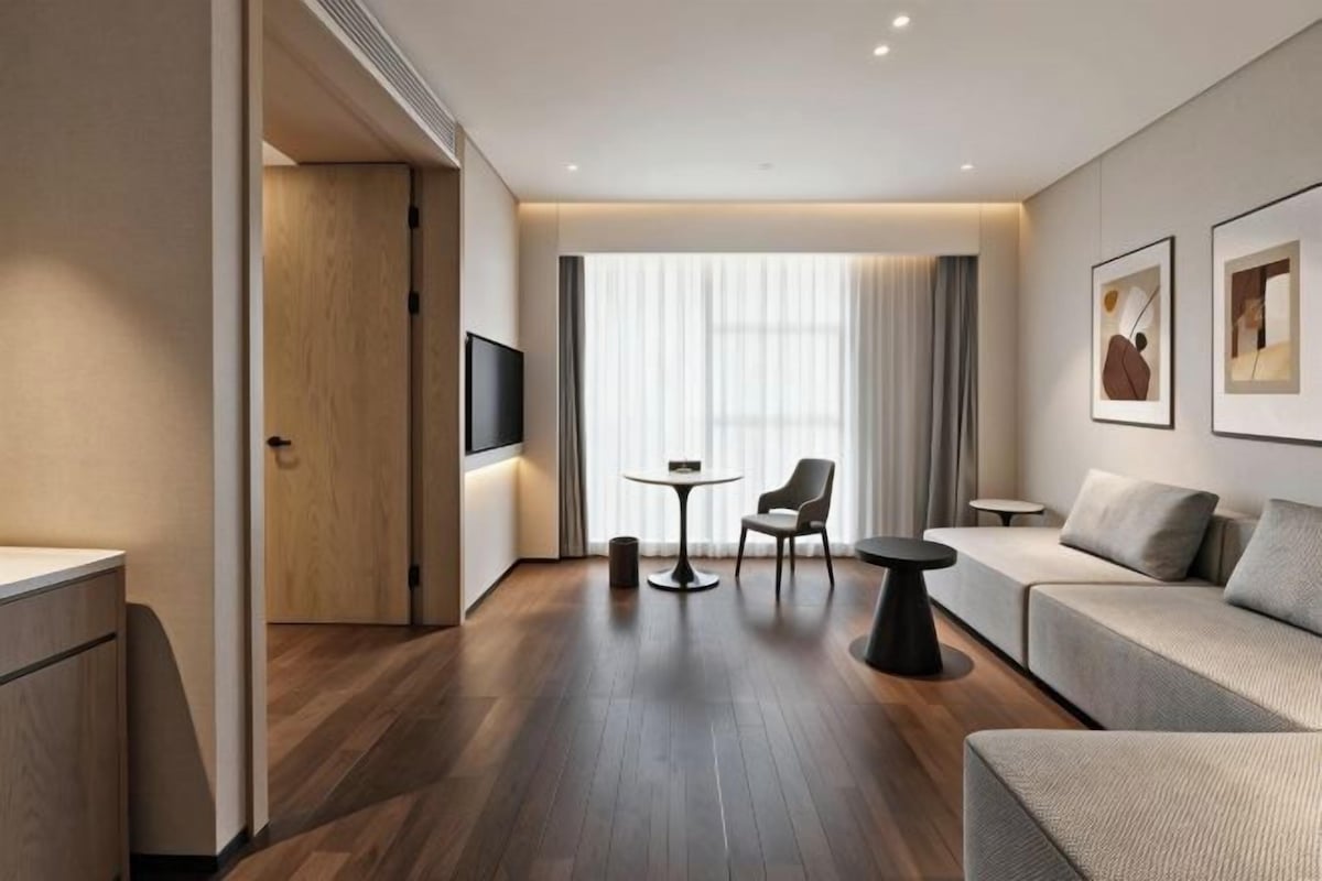 A modern hotel room with a sofa, a small table, and a TV mounted on the wall.