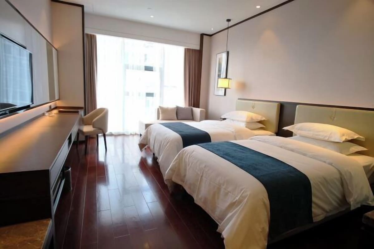 A hotel room with two beds, a desk, a chair, and a TV.