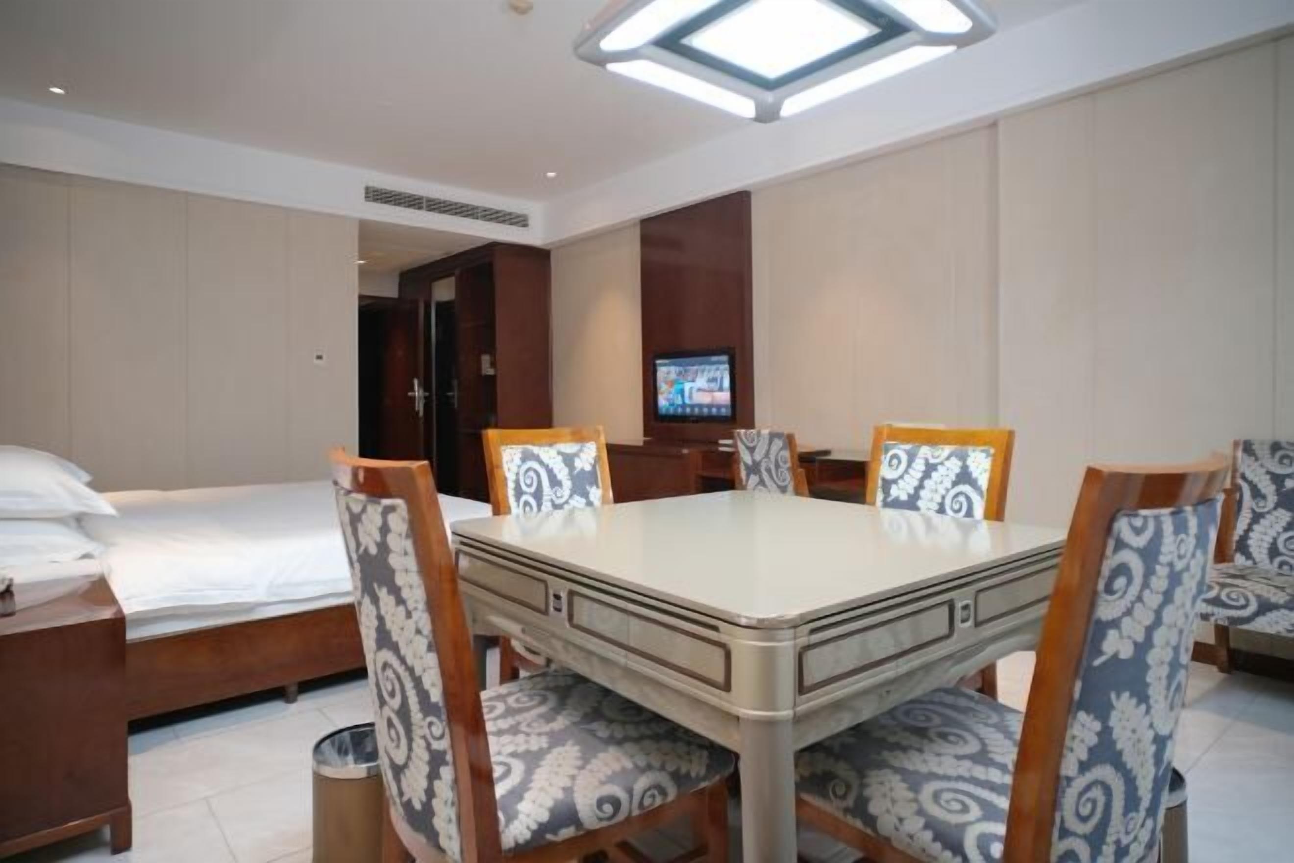 Una habitación de hotel con una mesa de comedor, cuatro sillas, un televisor, una cama y un cubo de basura.