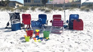 Beach chairs, umbrellas, and beach toys on a sandy beach with houses in the background. - Townhome Steps to the Beach · Resort Pool & Courts (Panama City Beach)
