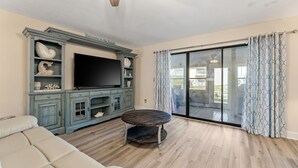 A living room with a flat-screen TV, a wooden coffee table, a beige sofa, and a sliding glass door leading to a balcony. - Townhome Steps to the Beach · Resort Pool & Courts (Panama City Beach)