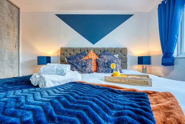 A hotel room with a large bed, a headboard with a geometric design, and a tray with orange juice and a lemon.