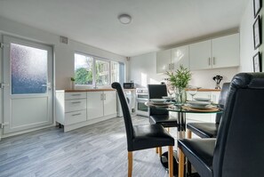 A modern kitchen with white cabinets, a dining table set for four, and a large window providing natural light.