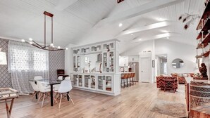 A spacious living area with a dining table, white chairs, a kitchen with white cabinets, and a wooden floor. - Stylish Cozy Cottage in East~10 min. to Broadway (Nashville)