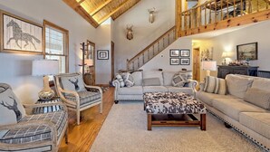 A spacious living room with a high wooden ceiling, a staircase, and a deer head mounted on the wall. - The Gathering Place by Chatuge Home Concierge | Mountain Views · Lake Chatuge Views (Hiawassee)