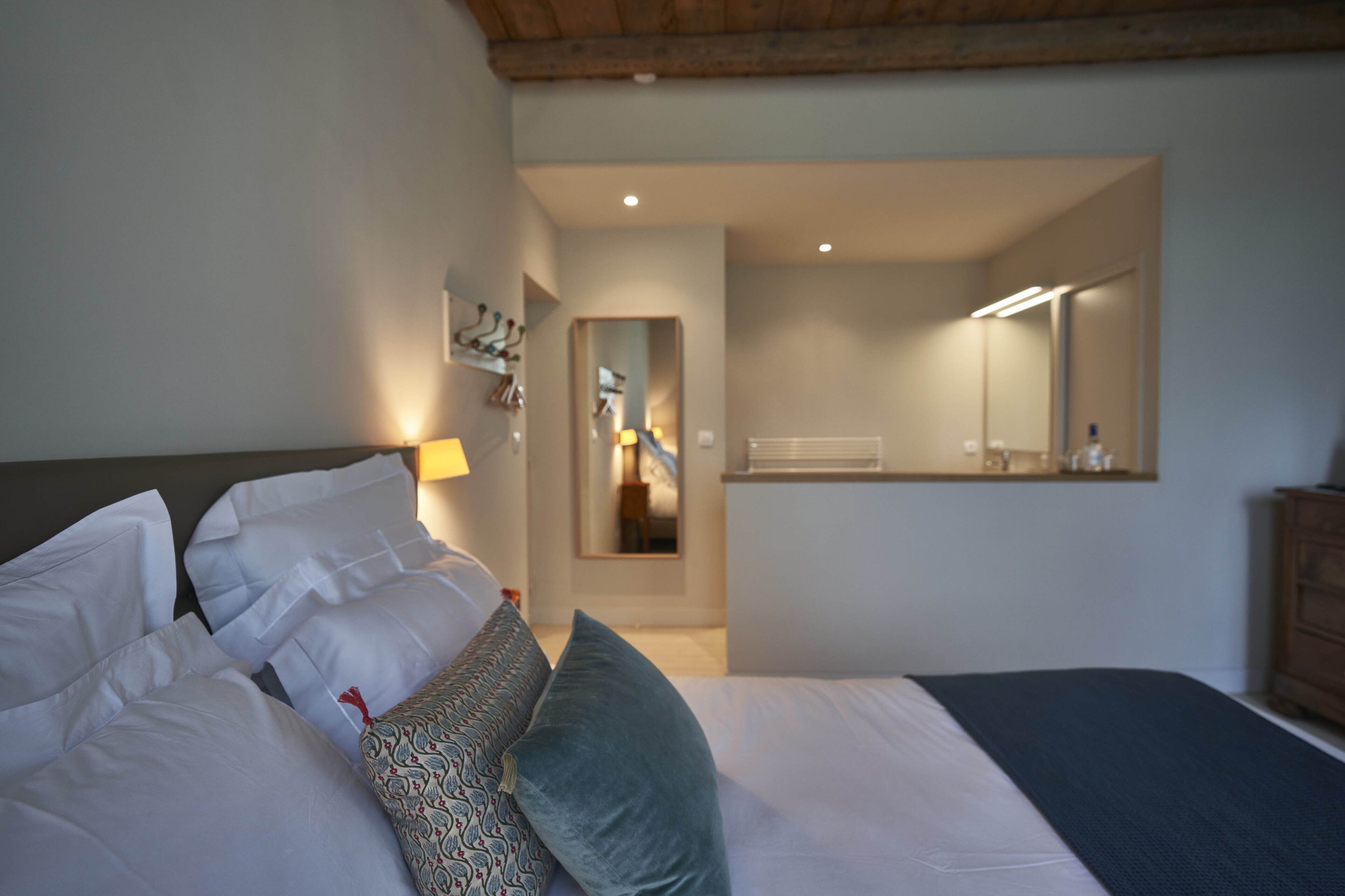 A bedroom with a bed, pillows, a bedside table, a mirror, and a wooden headboard.
