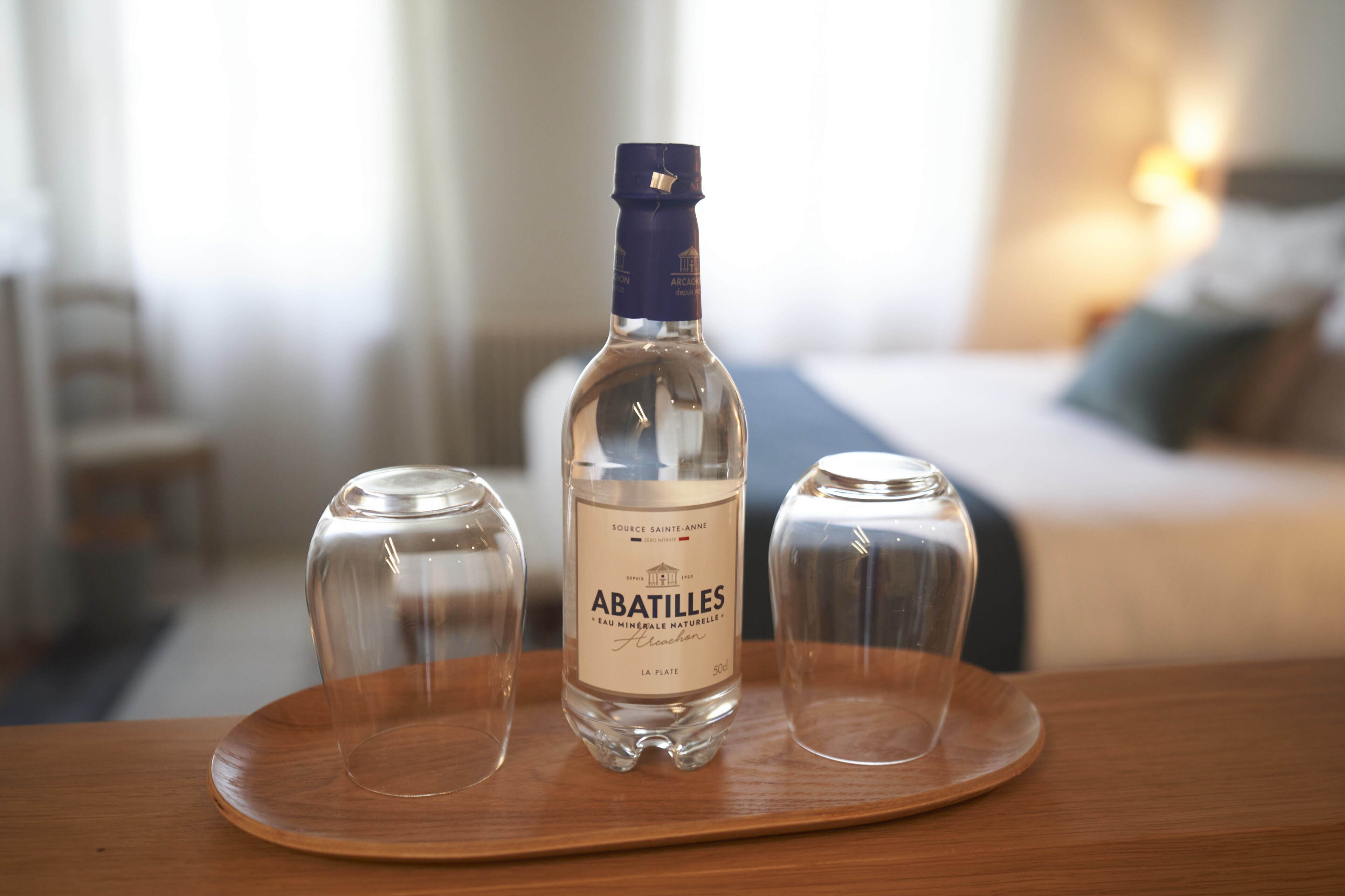 A bottle of Abatilles mineral water on a wooden tray with two glasses.