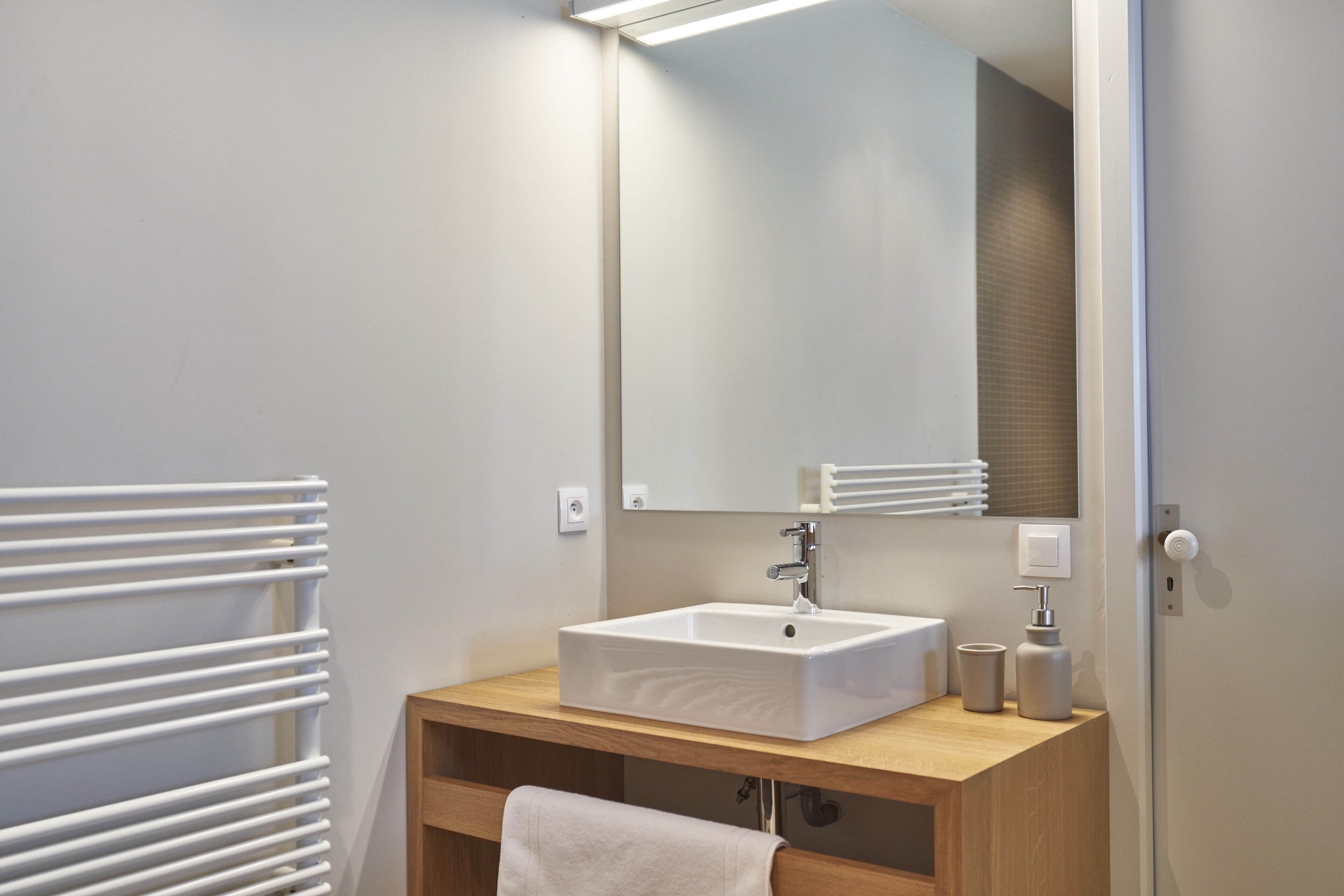Un baño moderno con lavamanos, espejo y toallero blancos.