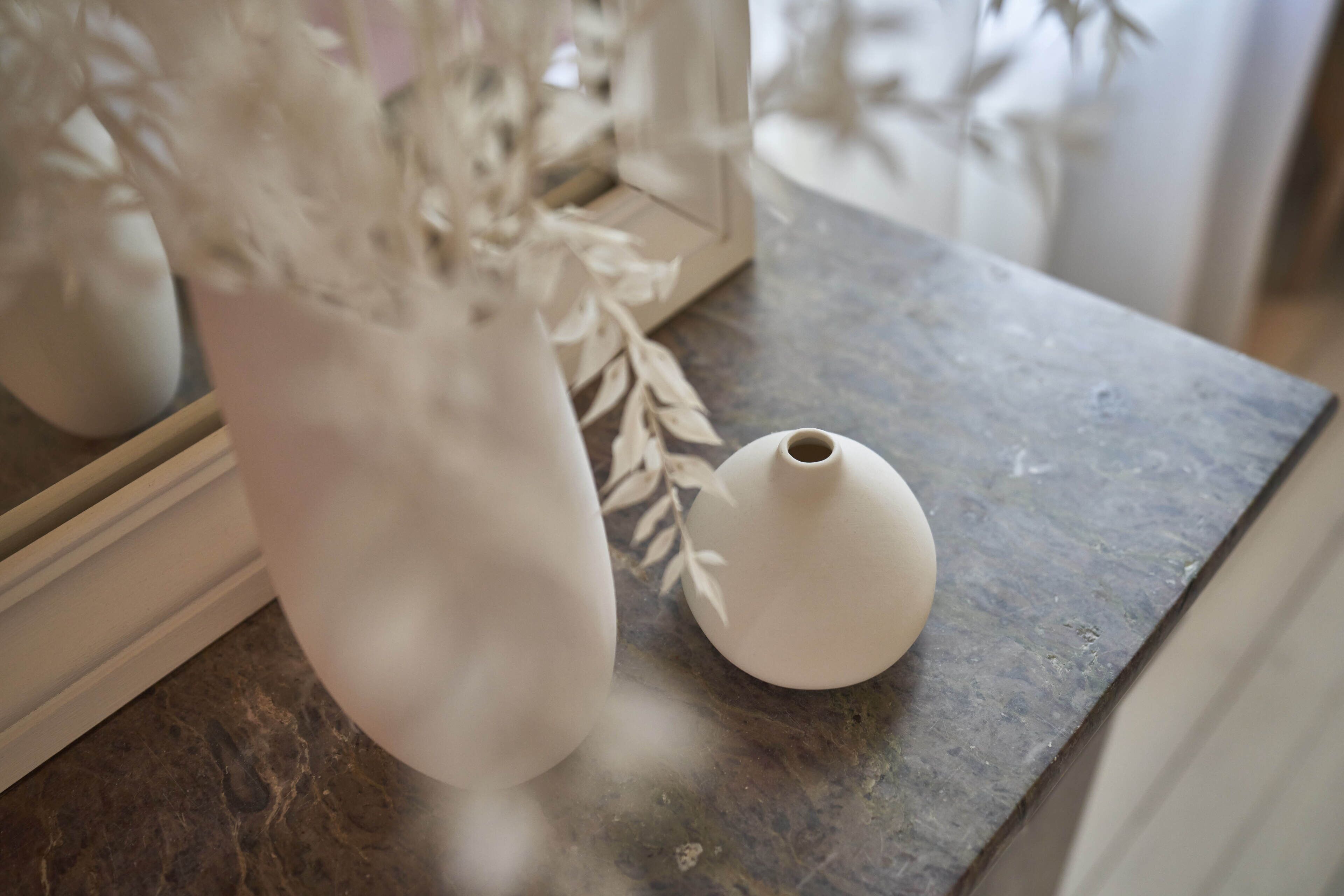 A marble countertop with two white ceramic vases and a decorative leaf arrangement.