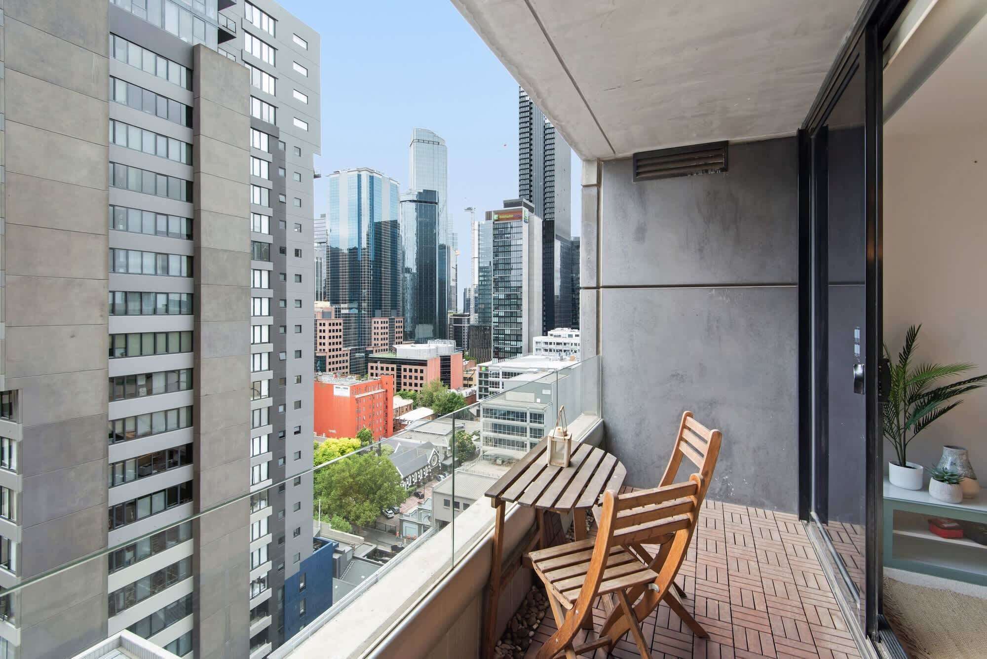 A balcony with a table and chairs, overlooking a cityscape with high-rise buildings.