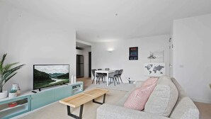 Ein modernes Wohnzimmer mit Flachbildfernseher, einer Couch, einem Essbereich mit Stühlen und einem kleinen Tisch.