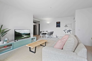 A modern living room with a flat-screen TV, a sofa, a dining area with chairs, and a small table.