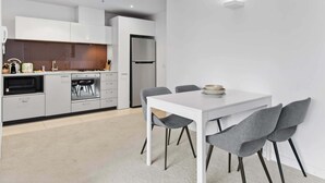 Eine moderne Küche mit weißen Schränken, einem eingebauten Ofen und einem Kühlschrank. Es gibt einen Essbereich mit einem weißen Tisch und grauen Stühlen.