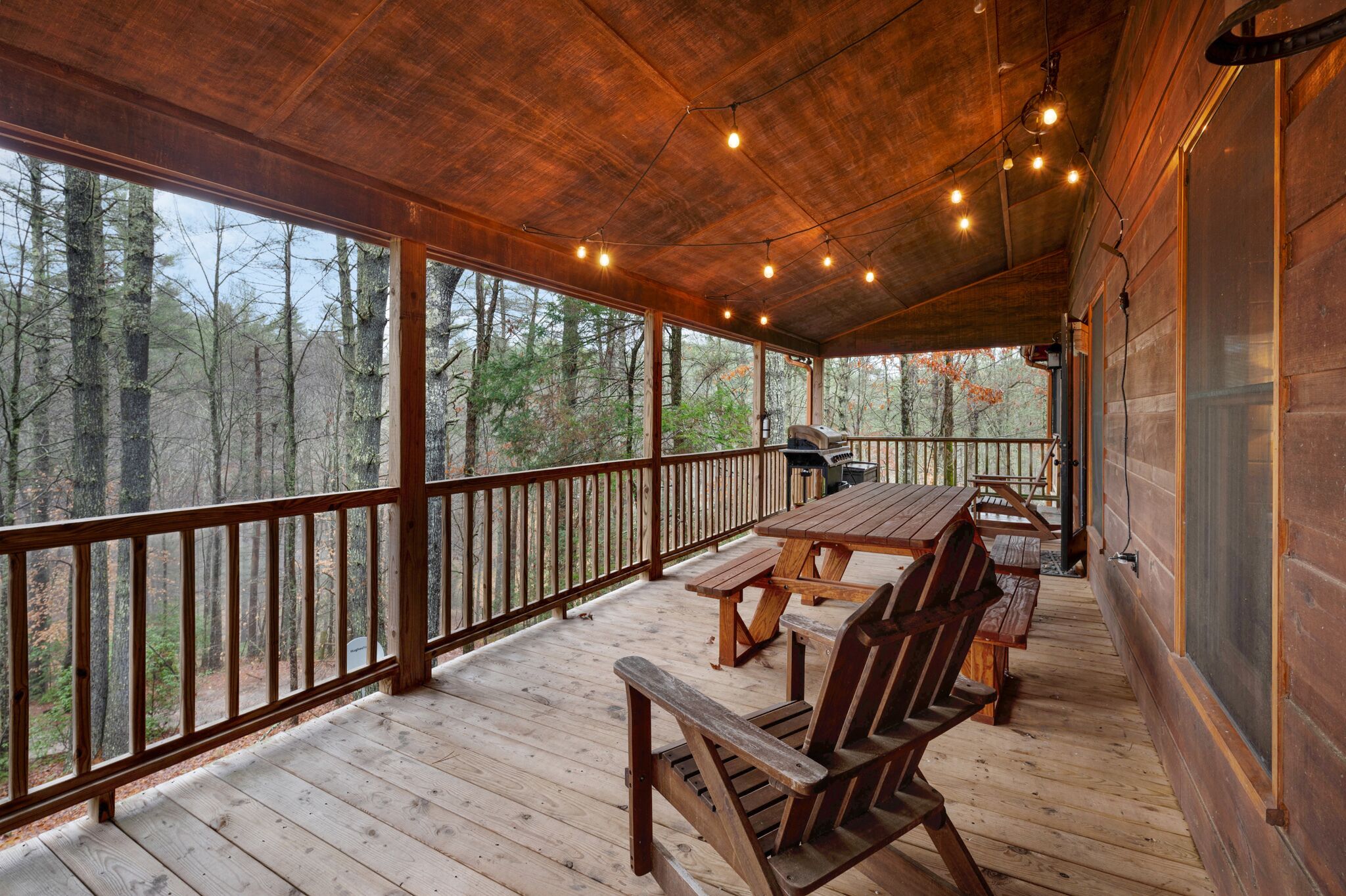A wooden deck with a table and benches, overlooking a forested area.