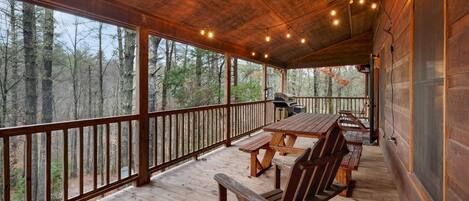 A wooden deck with a table and benches, overlooking a forested area.