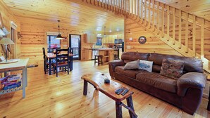 A wooden interior with a staircase, a brown leather sofa, a dining table, and a kitchen area. - Storybook Hideaway, where memories that fill your heart with comfort, gladness a (Blue Ridge)