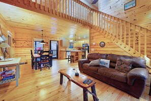 A wooden interior with a staircase, a brown leather sofa, a dining table, and a kitchen area.