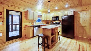 A wooden cabin-style kitchen with a central island, built-in appliances, and a door leading to an outdoor deck. - Storybook Hideaway, where memories that fill your heart with comfort, gladness a (Blue Ridge)
