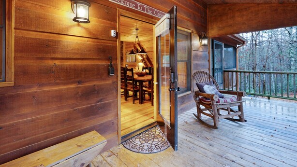 A wooden cabin with a 'Welcome To The Cabin' sign, a dining area with a table and chairs, and a rocking chair on the porch. - Storybook Hideaway, where memories that fill your heart with comfort, gladness a (Blue Ridge)