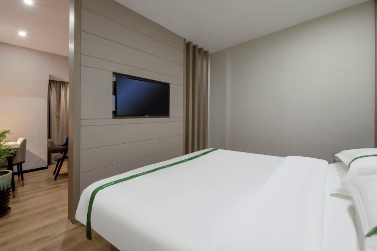 Una habitación de hotel con una cama, un televisor montado en la pared y un escritorio con una silla.