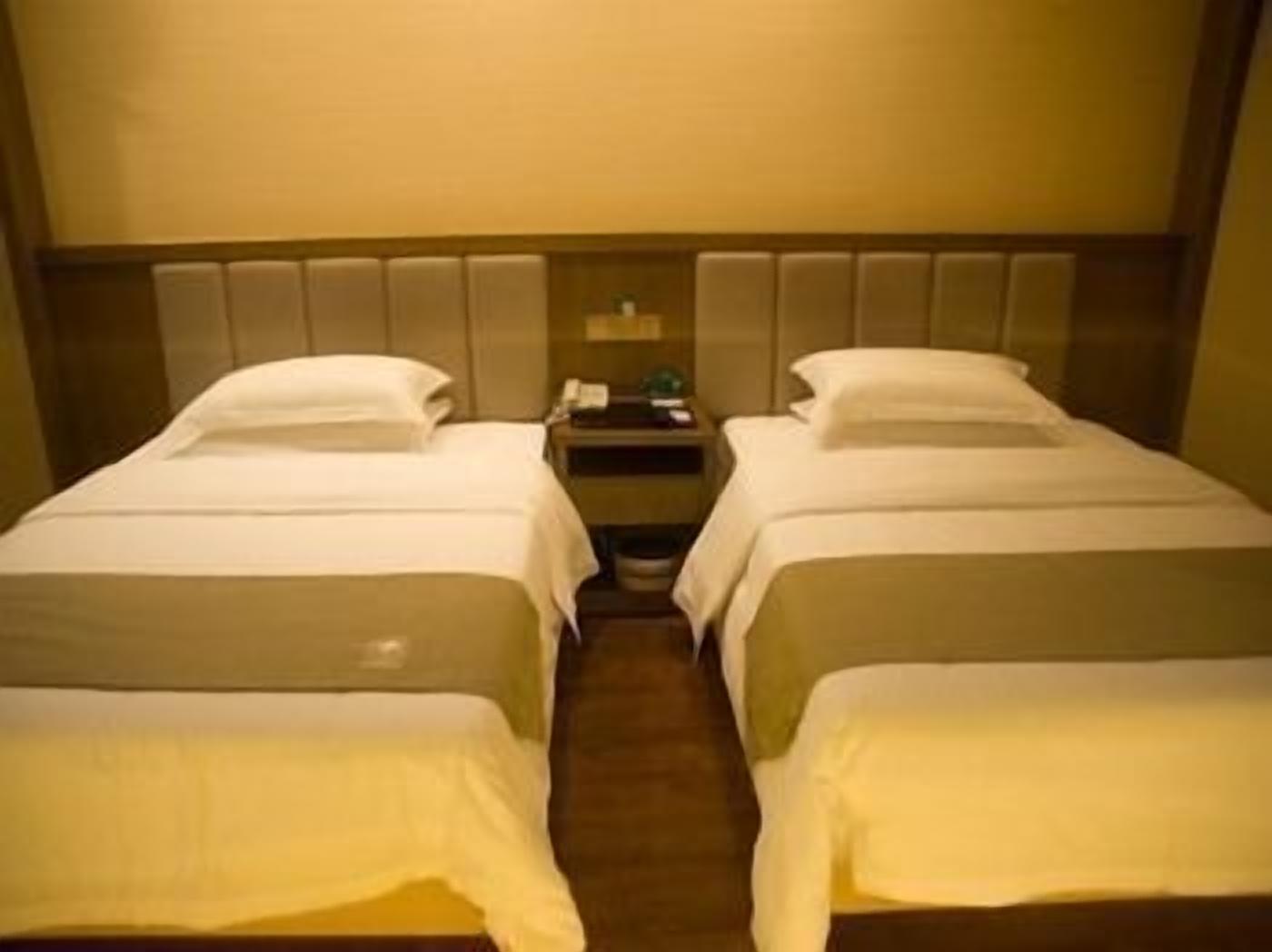 A hotel room with two single beds, a nightstand, and a wall-mounted telephone.