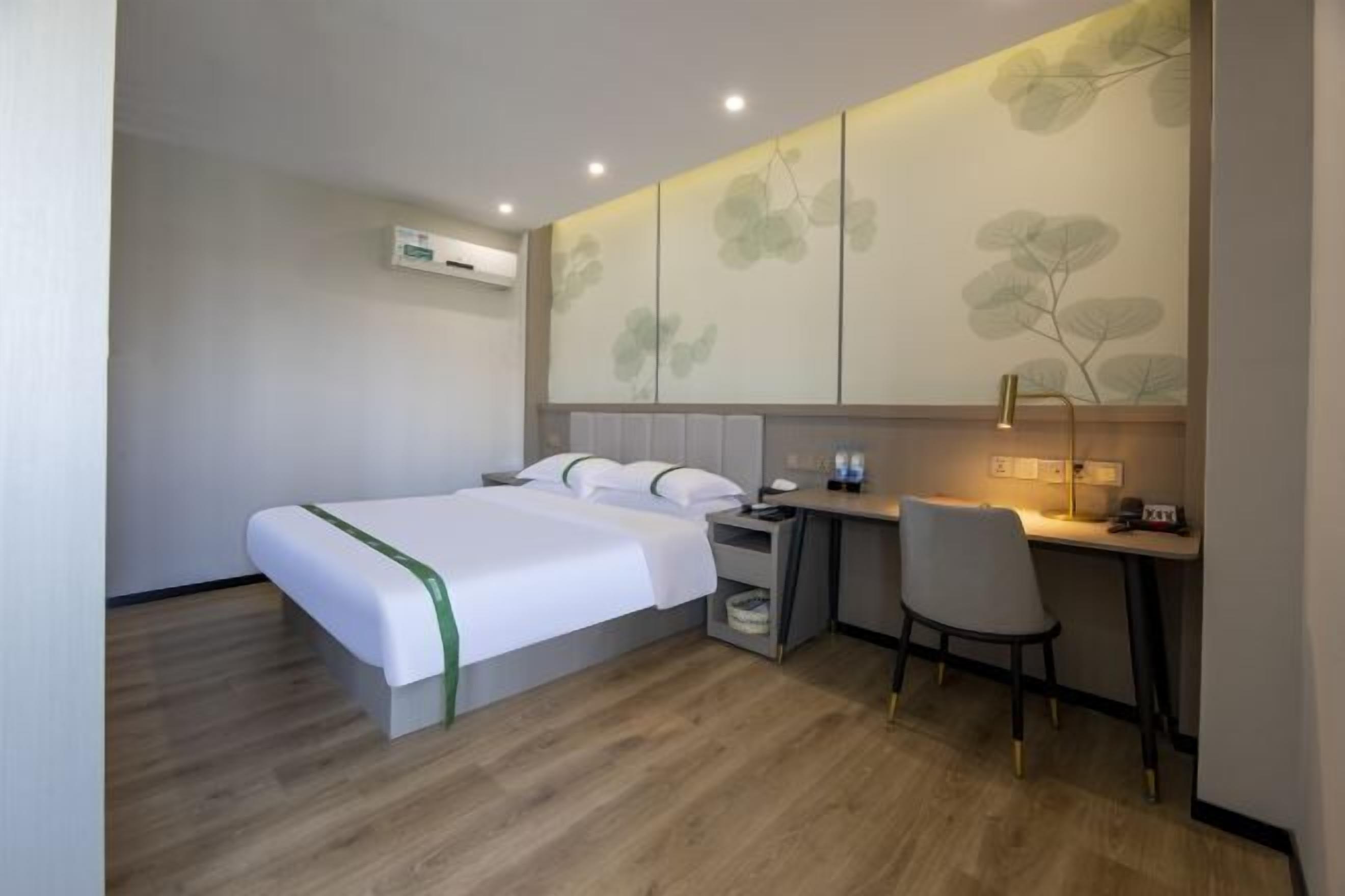 A hotel room with a bed, a desk, and a chair. There is an air conditioning unit on the wall.