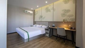 A hotel room with a bed, a desk, and a chair. There is an air conditioning unit on the wall.
