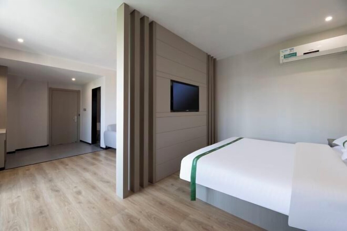 A hotel room with a bed, a television mounted on the wall, and a wooden floor.