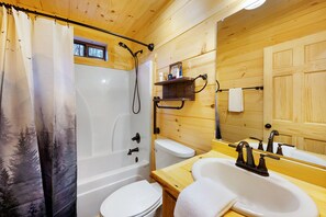 Een houten badkamertje met een bad, toilet en wastafel.