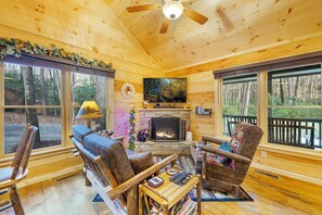 A cozy cabin interior with a fireplace, wooden furniture, and large windows offering a forest view. - Trail Side Retreat, great cabin for small family vacation, honeymoon, or peacefu (Blue Ridge)