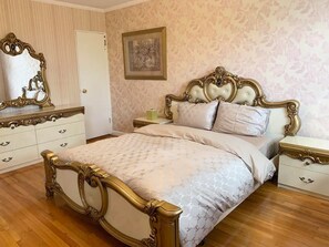 A bedroom with a large bed, ornate headboard, a dresser, a nightstand, a mirror, and a framed picture on the wall.
