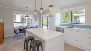 Cozinha moderna com ilha central, banquetas, iluminação pendente e vista para o exterior.